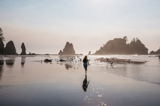 young female runs into flock of birds on beach
