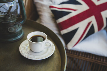A cup of black coffee on an iron table and an armchair with a pillow with a picture of the flag of Great Britain. Retro English style.