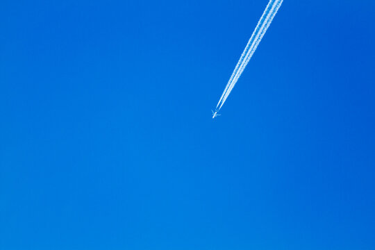 White contrail and tiny airplane against blue sky on a sunny day looking up