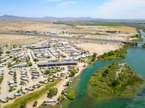 a stunning aerial shot of the deep green water of the Colorado River, the lush green trees, boats on the water and buildings with blue sky at Queshan Park in Blythe California