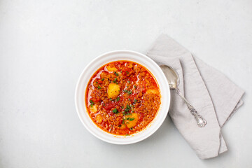 Top View of Vegan Vegetable Soup in a White Bowl on a Gray Countertop with a Gray Napkin and Silver Spoon