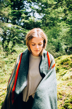 Young Blonde Woman Wrapped In Wool Blanket Standing In Mossy Wooded Area