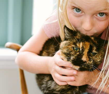 A little girl loving her pet cat just a little too much.