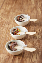 Various chocolate pops decorated with ribbon and sprinkles on a brown wood background.