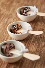 Various chocolate pops decorated with ribbon and sprinkles on a brown wood background.
