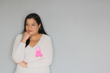Obraz premium Latin woman with pink ribbon in hands and plain gray background for campaign against breast cancer