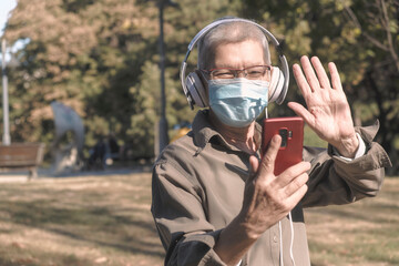 Senior old woman listening to her favourite music through big headphones, with mask on
