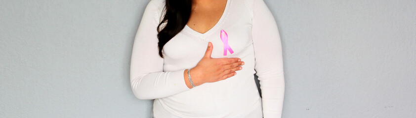 woman with pink ribbon in her hands and plain gray background for campaign against breast cancer