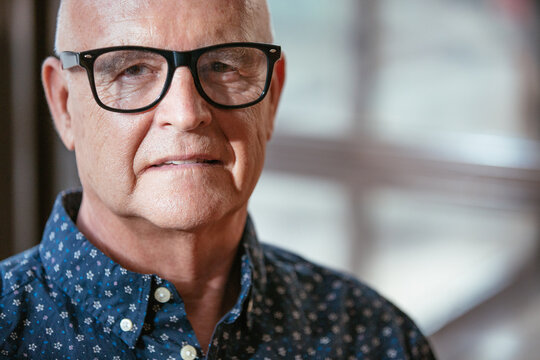 Trendy senior man portrait, wearing glasses and a dark blue shirt looking at the camera.