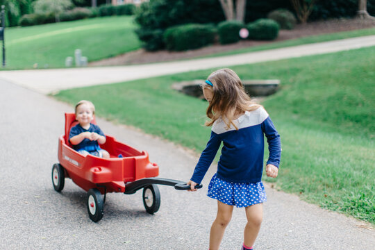 Cute big sister pulling her baby brother in a wagon
