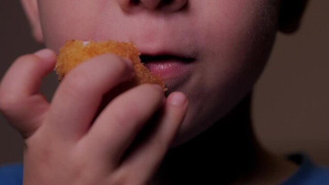 Cute little caucasian child eating fast food. Hungry child bites naggins, breaded colmar. Small kid in a fast food home eats. Close up portrait of a little baby boy eating lunch.