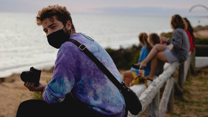 Photographer sitting looking at camera with people behind on the beach.