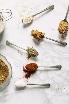 Herbs and spices on spoons on a marble background.