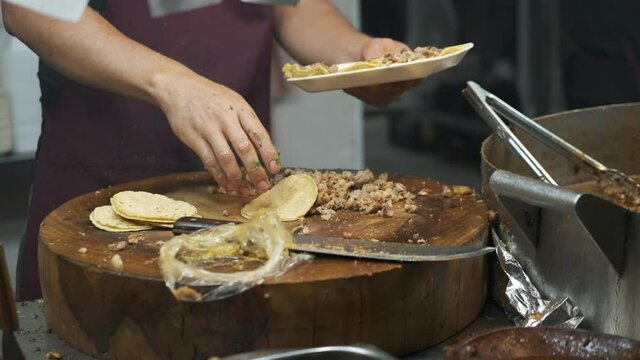 A man is putting tacos on a plate in a mexican street food restaurant