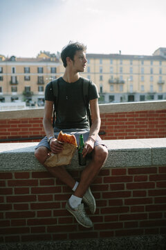 Young man eating pizza and drinking a beer outdoors