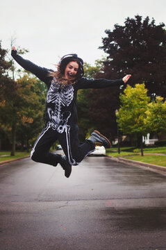 A young woman wearing a skeleton onesie jumping in the air