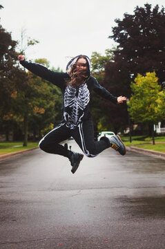 A young woman wearing a skeleton onesie jumping in the air