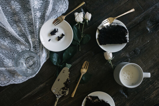 Slices of chocolate cake, white mini roses and glass of milk styled on lace and dark wood table