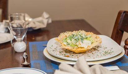 Seasoned and plated Caesar salad on an edible parmesan basket on a white plate and decorated table.