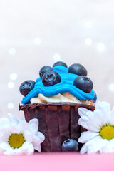 cupcake with a cheerful blue cream decorated with blueberries and chamomile flowers. close up