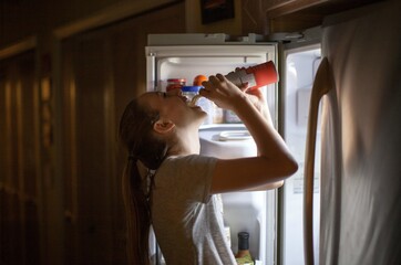 Teenage girl standing at the refrigerator spraying whip cream into her mouth