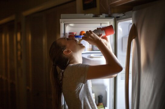 Teenage girl standing at the refrigerator spraying whip cream into her mouth