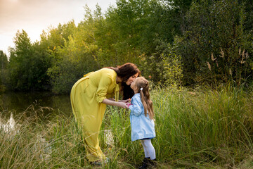 Pregnant woman in yellow dress with her daughter in nature