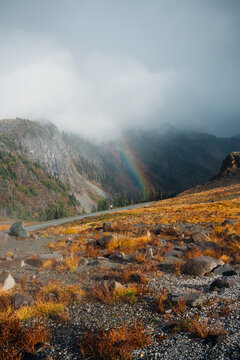 Rainbow And Dark Clouds Over Rocky Mountainside
