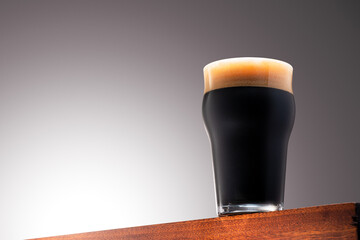 Close up photo of a Glass of dark beer on a Wooden Surface and Gradient Background