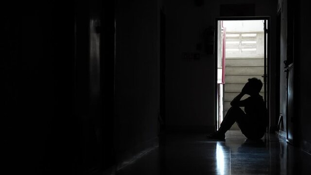 Silhouette of a sad man sitting in the dark leaning against the wall in old condo, Domestic violence, family problems, Stress, violence, The concept of depression and suicide