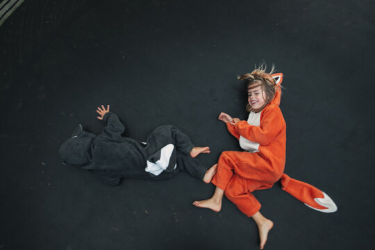 Cute girl in fox and boy in raccoon costume playing on trampoline