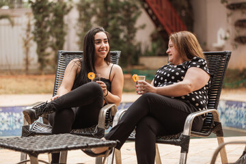 Adult daughter and mother talking and drinking juice outside the house