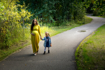 Obraz premium Pregnant woman in yellow dress with her daughter in nature