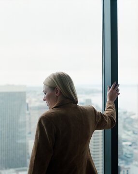 Female executive looking out large office window towards city