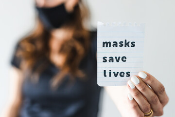 covid-19 pandemic outbreak, woman holding Masks save lives text towards the camera shot at shallow depth of field