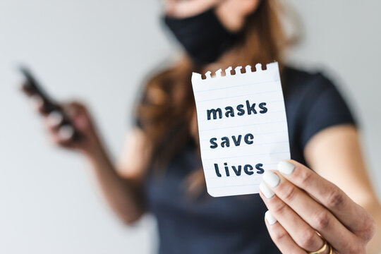 Covid-19 Pandemic Outbreak, Woman Holding Masks Save Lives Text Towards The Camera While Browsing On Her Smartphone