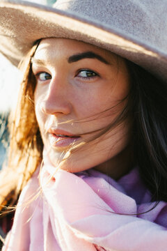 Closeup portrait of a young woman wearing a hat and a pink scarf.