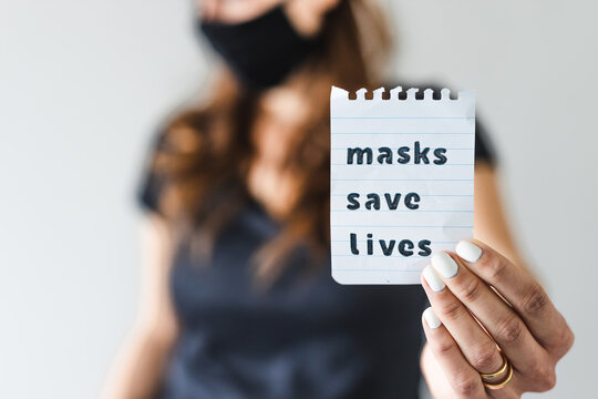 covid-19 pandemic outbreak, woman holding Masks save lives text towards the camera shot at shallow depth of field - Powered by Adobe