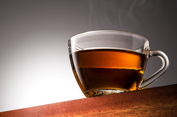 Close up photo of a Glass cup of tea on a Wooden Surface and Gradient Background
