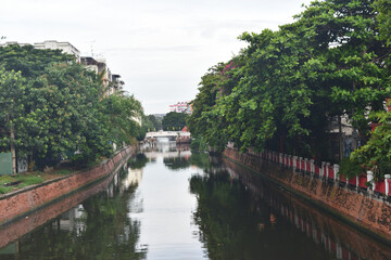 Fototapeta na wymiar Canal with brown brick walls and green plants reflecting on the water surface, View from the bridge in Bangkok, Thailand