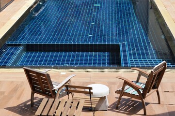 Vintage wooden chairs at the edge of a blue swimming pool in summer sunshine