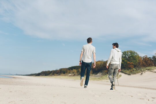 Young men walking on beach on sunny day with sand dunes.