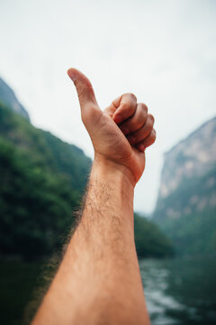 Close up of a male hand doing a thumbs up with a scenic view of canyon and lake in Chiapas, Mexico. POV view