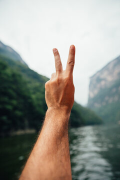 Close up of a male hand making the victory sign with a scenic view of canyon and lake in Chiapas, Mexico. POV view