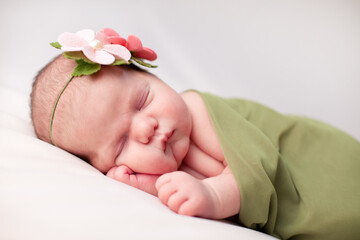 Newborn Baby Girl Sleeping Peacefully in Green Blanket, Wearing Flower Headband, Spring