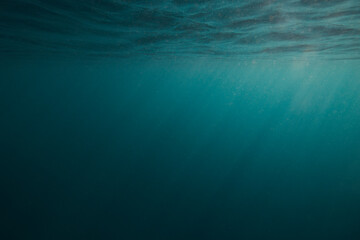 Dark blue under water empty sea background with sunrays going trough the surface