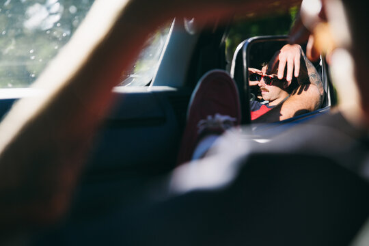 Car mirror view of young man in copilot seat resting while a road trip