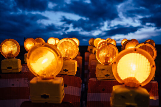 Two dozen illuminated, flashing road construction barricade signs in front of a dramatic sky.