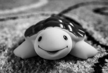 Grayscale shot of a plastic toy turtle on soft carpet