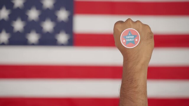 Rising fist with I voted early sticker on hand with US flag as background - Concept of early voting at US election.